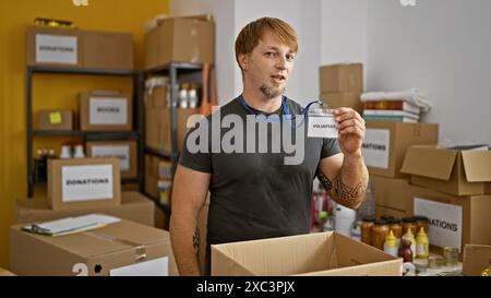 Hübscher junger Mann, der freiwillig in einem Lagerhaus Spenden sortiert und eine Marke hält. Stockfoto