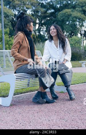 Vertikales Bild für soziale Netzwerke von zwei lateinischen Frauen, die den Nachmittag im Park genießen, eine mit brauner Jacke und die andere mit W Stockfoto