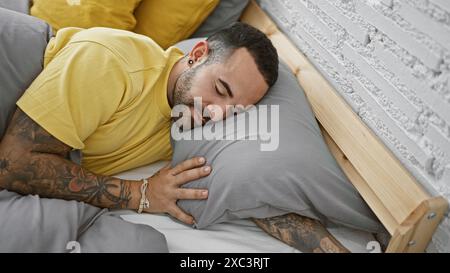 Hübscher hispanischer Mann mit Bart und Tattoos, der friedlich in einem modernen Schlafzimmer schläft Stockfoto