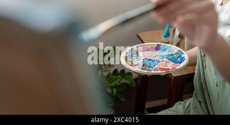 Künstlermalerei in Werkstatt mit farbenfroher Palette und Pinsel, kreatives Studio-Umfeld, künstlerischer Prozess, Nahaufnahme von Hand und Farbe, inspirierende Kunst Stockfoto