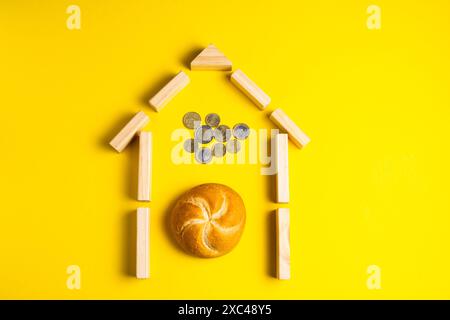 Hand hält Geldmünzen in der Nähe von Brot auf gelbem Hintergrund Stockfoto