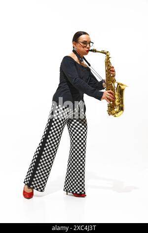 Das durchgehende Porträt der eleganten älteren Frau, Saxophonistin in karierten Hosen, spielt intensiv isoliert auf weißem Hintergrund Stockfoto