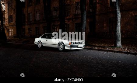 Silbernes klassisches BMW 6er E24 Coupé bei Nacht in der Altstadt. Vorderansicht eines 1980er-BMW mit runden Scheinwerfern. Stockfoto