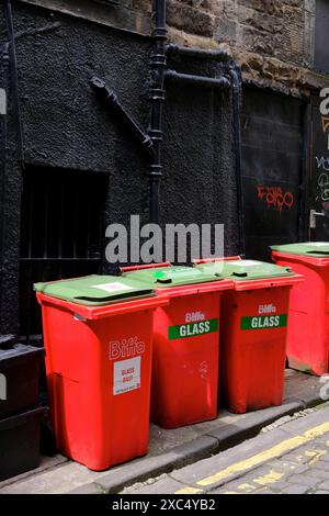 Rote, kommerzielle Recyclingbehälter aus Glas mit grünem Deckel, die vor einer schwarzen Wand außerhalb von angeordnet sind Stockfoto