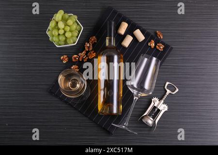Flügelkorkenzieher, Flasche Wein, Gläser, Korken, Walnüsse und Trauben auf schwarzem Tisch, Blick von oben Stockfoto