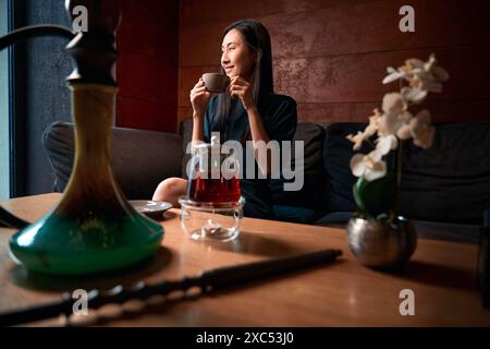 Positive asiatische Frau, die aufrichtig lacht und eine Tasse warmen Tee hält Stockfoto