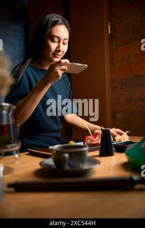 Asiatische Food-Bloggerin, die ein Foto von elegant serviertem Sushi-Set macht Stockfoto