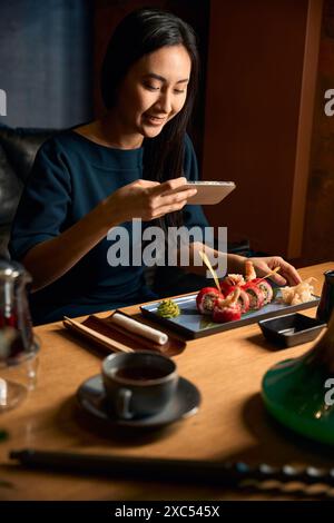Lächelnde asiatische Bloggerin, die ihr leckeres frisches Sushi fotografiert Stockfoto