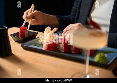 Frau, die Sushi mit Essstäbchen hält und in Sojasauce taucht Stockfoto