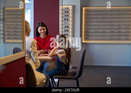 Der Manager hilft, eine Brille für ein kleines Mädchen auszuwählen Stockfoto