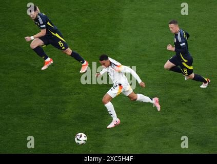 Jamal Musiala (Mitte) in Aktion mit dem schottischen Kieran Tierney (links) und Callum McGregor während des Gruppenspiels der UEFA Euro 2024 in der Münchner Fußball-Arena. Bilddatum: Freitag, 14. Juni 2024. Stockfoto