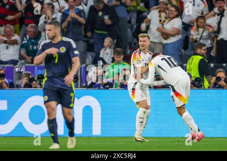 München, Deutschland. Juni 2024. Fußball, UEFA Euro 2024, Europameisterschaft, Deutschland - Schottland, Vorrunde, Gruppe A, Spieltag 1, Football Arena München. Maximilian Mittelstädt (Mitte) und Jamal Musiala (rechts) feiern nach 2:0, Schottland John McGinn auf der linken Seite. Quelle: Christian Charisius/dpa/Alamy Live News Stockfoto