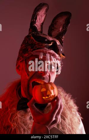 Gruseliger Hasenmann, junger Mann in einer gruseligen Hasenmaske, mit Kürbiskerzenleuchter, Thema der Angst und des Horrors in Verbindung mit Maske und Gesichtsausbrüchen Stockfoto