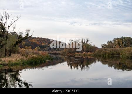 Siwerskyi Donets Flussufer in der Ukraine mit Herbstbäumen und wolkigen Himmelsreflexen Stockfoto