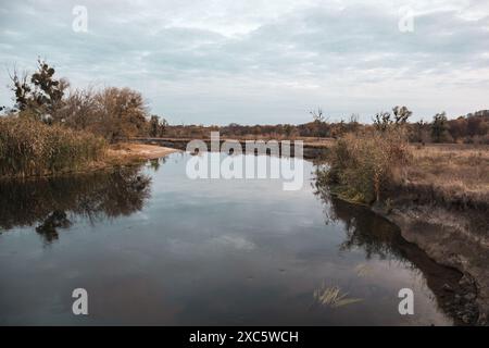Ruhige Flussbiegung in der Ukraine mit herbstlicher Natur und bewölkten Himmelsreflexen auf der Wasseroberfläche Stockfoto