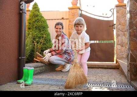 Mutter und ihre süße Tochter putzen zusammen in der Nähe des Hauses am Frühlingstag Stockfoto