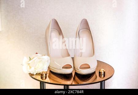 Beige High-Heels Peep-Toe-Schuhe auf einem goldenen Tisch mit weißer Rose schaffen eine elegante und zarte Brautatmosphäre Stockfoto