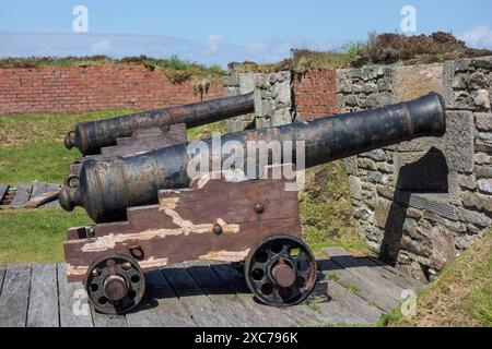 Zwei alte Kanonen stehen auf Holzregalen in einer Festung neben einer Steinmauer, lerwick, shetlands, Schottland, Großbritannien Stockfoto