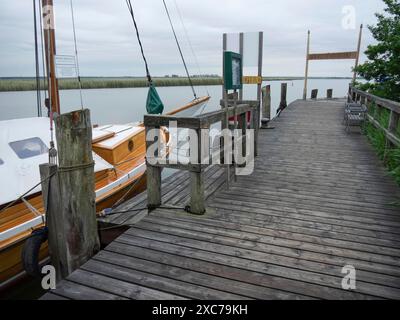 Holzsteg und ein verankertes Segelboot, das sich in einen ruhigen See, bewölkten Himmel, zingst, ostsee, deutschland ausdehnt Stockfoto