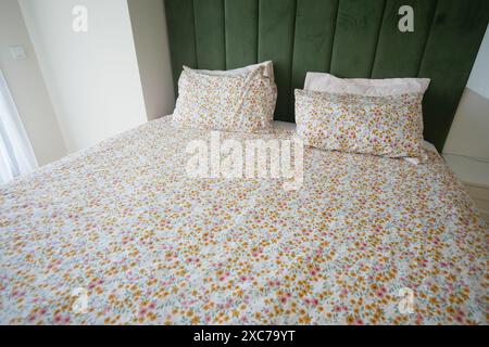 Ein Bett mit geblümter Bettwäsche in einem Schlafzimmer mit Hartholzfußboden und gemütlicher Bettwäsche Stockfoto