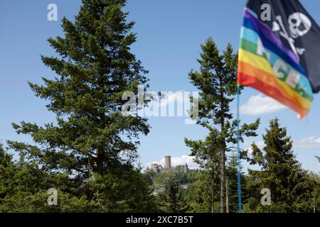 Adenau, Deutschland, 8. Juni 2024: Im Hintergrund ist die Nürnburg zu sehen, während eine Regenbogenfahne und eine Piratenfahne auf einem Zelt an einem der Felsen am Himmel fliegen Stockfoto