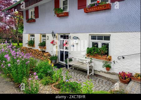 Holzschindelfassade mit Brennholzhaufen und Blumenschmuck in Eisenbach, Kreuzthal, Markt Buchenberg, Allgäu, Schwaben, Bayern, Deutschland Stockfoto