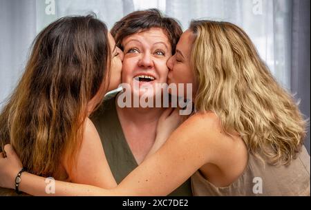 Erwachsene Töchter küssen ihre Mutter von verschiedenen Seiten. Zusammengehörigkeit Stockfoto