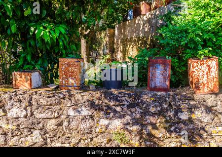 Alykes, Zakynthos Griechenland 24. Mai 2024 - Alte rostige Dosen sitzen auf einer Steinmauer in Zakynthos mit Büschen im Hintergrund Stockfoto