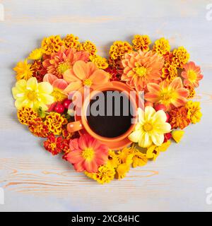 Zusammensetzung aus roter Kaffeetasse und Dahlien, Ringelblumen in Herzform auf blauem Holzhintergrund. Flache Lagen. Stockfoto