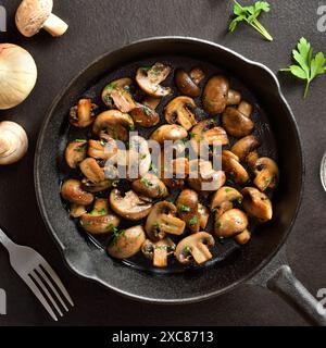 Gerösteter Pilz in gusseiserner Pfanne auf dunklem Steinhintergrund. Vegetarisches veganes Lebensmittelkonzept. Draufsicht, flach Stockfoto