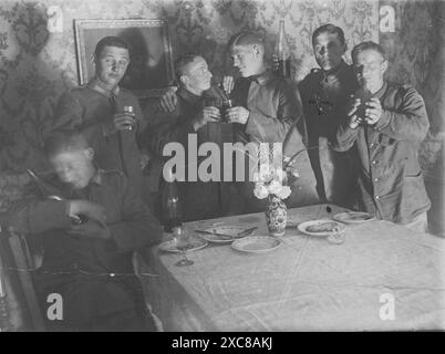 Ein Schwarzweiß-Foto, das eine Gruppe von sechs deutschen Soldaten in einem Speisesaal zeigt, wahrscheinlich während des Ersten Weltkriegs oder früher gefangen genommen. Die Soldaten sitzen an einem Tisch, unterhalten sich zwanglos und genießen Drinks. Stockfoto