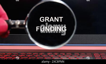 Konzept für die Finanzierung von Unternehmen und Zuschüssen. Kopierbereich. Die Worte GRANT FUNDING Text erschien durch eine Lupe auf einem dimmeren Laptop Bildschirm Stockfoto