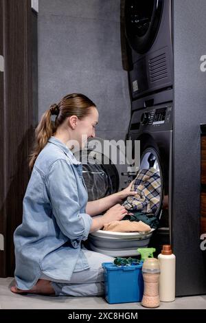 Die junge Frau nimmt die gewaschenen Kleider zu Hause aus der Waschmaschine. Stockfoto