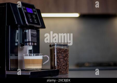Moderne Kaffeemaschine mit Glasbecher Latte in der Küche. Stockfoto