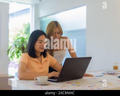 Zwei Frauen im Café, die zusammen einen Laptop benutzen und so aussehen, als würden sie an einem Projekt arbeiten Stockfoto