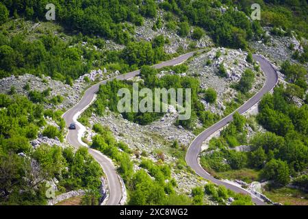 Blick von oben auf eine kurvenreiche Straße, auf der sich ein Auto bewegt. Bergserpentine, die zum Dorf Vrbanj (Gemeinde Herceg Novi, Montenegro) führt Stockfoto