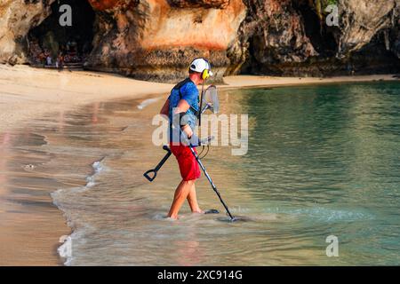 Kaukasier mit einem Metalldetektor im blauen Wasser des Phra Nang Cave Beach auf der Railay Peninsula in der Provinz Krabi, Thailand Stockfoto