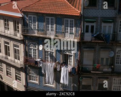 Die alte Frau hängt ihre frisch gewaschene Wäsche und Kleidung vor ihrem Balkon auf. Bunte Gebäudefassade. Porto.Portugal 29.05.2024 Stockfoto