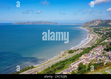 Hohe Aussicht auf Dorf, Strand und A55 Expressway Straße an der Küste mit Great Orme in der Ferne. Penmaenmawr, Conwy, Nordwales, Großbritannien Stockfoto