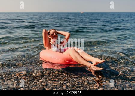 Eine Frau schwimmt auf einem roten Schlauchboot im Ozean. Sie lächelt und genießt das Wasser Stockfoto