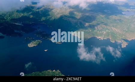 Aus der Vogelperspektive durch die Wolken zur Meeresbucht mit Küstenhügeln. Blick von oben von den Wolken zu den norwegischen Fjorden Stockfoto