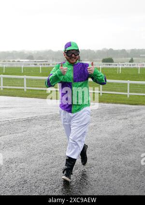 Ein als Jockey verkleideter Rennfahrer wird in einem Regenregen auf der Sandown Park Racecourse, Esher, gefangen. Bilddatum: Samstag, 15. Juni 2024. Stockfoto