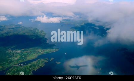 Luftaufnahme durch die Wolken zu den norwegischen Fjorden, Schatten eines Flugzeugs auf einer Wolke. Blick von oben von den Wolken auf die Meeresbucht mit Küstenhügeln Stockfoto