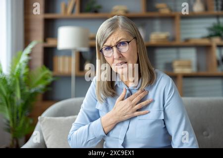 Ältere Frau bei einem Videoanruf mit einem Arzt, klagt über Schmerzen und sieht besorgt aus, während sie zu Hause sitzt Stockfoto