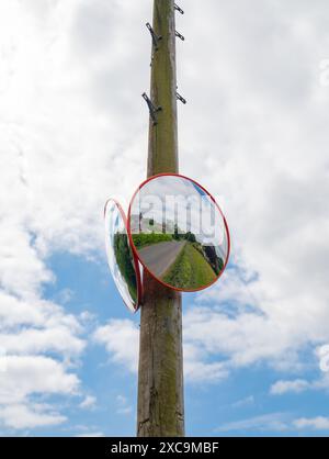 Zwei konvex-Spiegel an einem Telegrafenmast ermöglichen Sicht und Aufmerksamkeit beim Verlassen einer behinderten Einfahrt auf dem Land. Stockfoto