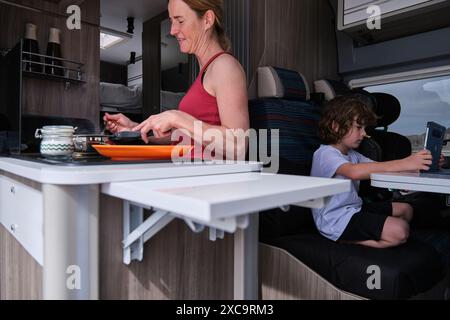 Eine Frau, die mit ihrem Sohn unterwegs ist, bereitet Essen zu, während der Sohn ein digitales Tablet verwendet Stockfoto
