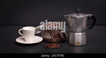 Espresso-Tasse, Mokakanne und ein Glas Kaffeebohnen auf schwarzer Schieferoberfläche. Kaffeekonzept. Stockfoto