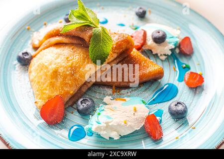 Hausgemachte Pfannkuchen oder Crepe suzette mit Erdbeeren, Heidelbeeren, Mascarpoen mit blauer curacao-Sauce auf blauem Teller. Nahaufnahme. Hochwertige Fotos Stockfoto
