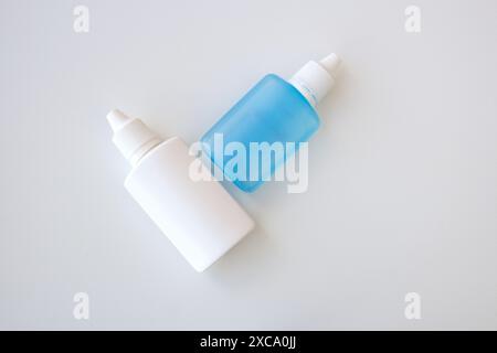 Zwei medizinische zusammendrückbare Plastiktropfflaschen auf weißem Hintergrund mit Platz für Kopie. Weiße und blaue Augentropfen. Stockfoto