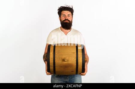 Ernsthafter bärtiger Mann mit einem Fass oder einem Fass Whiskey oder Wein. Weinbereitung. Schöner Mann mit Eichenfässern oder Bierfässern für Pub oder Bar. Brauer mit AA Stockfoto